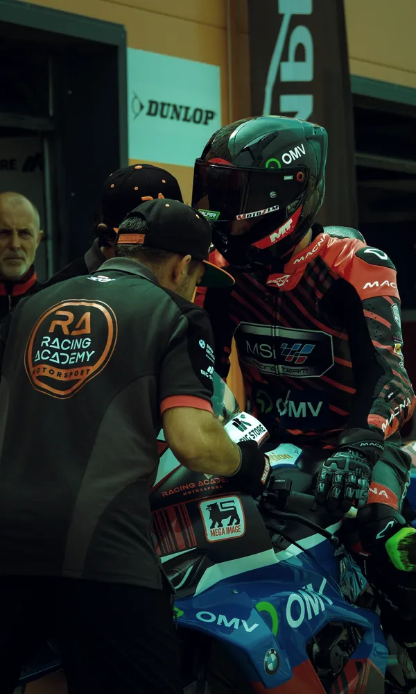 Un técnico del equipo habla con el piloto, ya subido en la moto, en el box
